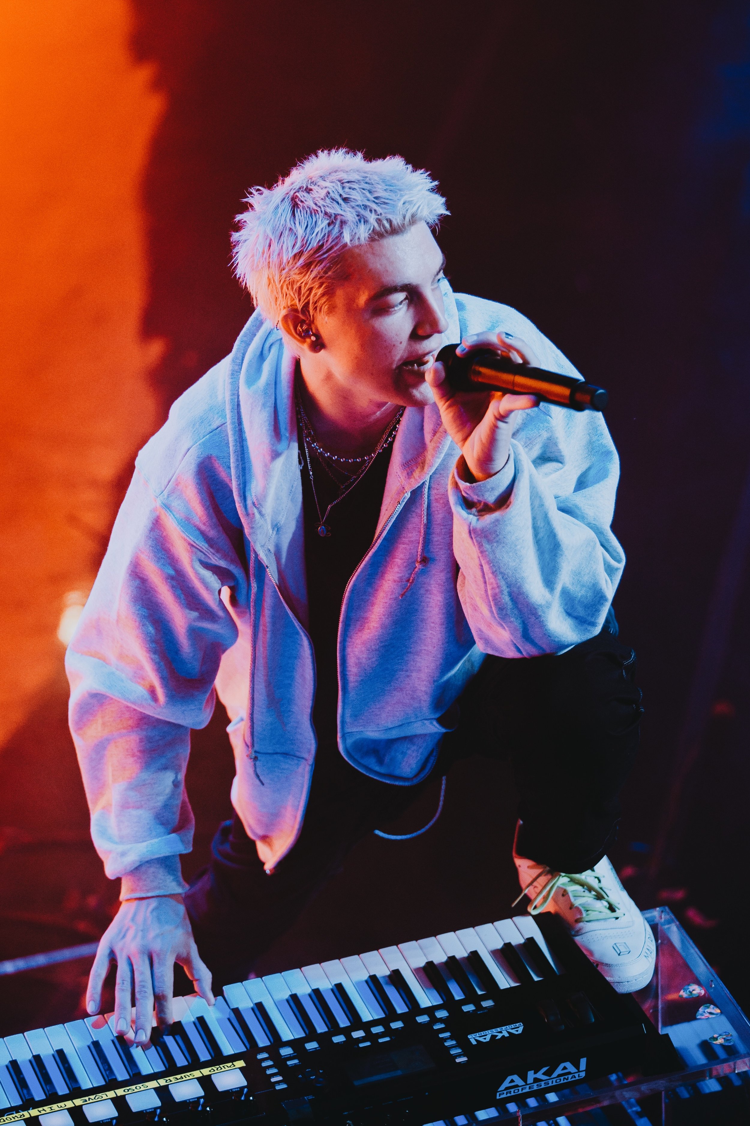The Interscope signed indie pop band’s frontman performs onstage, drenched in sunset colored lights. One hand clenches a microphone while the other plays a chord on the Akai keyboard in front of him. He plants one foot on the ground, while the other is adjacent to the keyboard. This is reminiscent of his carefully crafted ‘cool boy’ aesthetic.